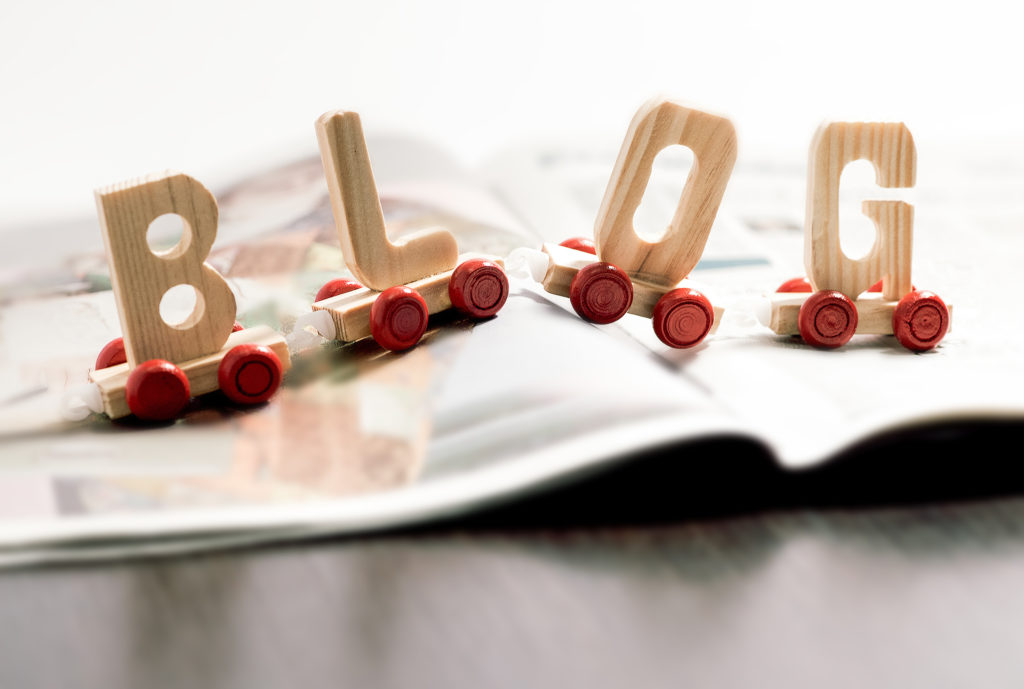 Word - Blog - in wooden letters on small red wheels spanning the pages of an open magazine in a communication and social media concept
